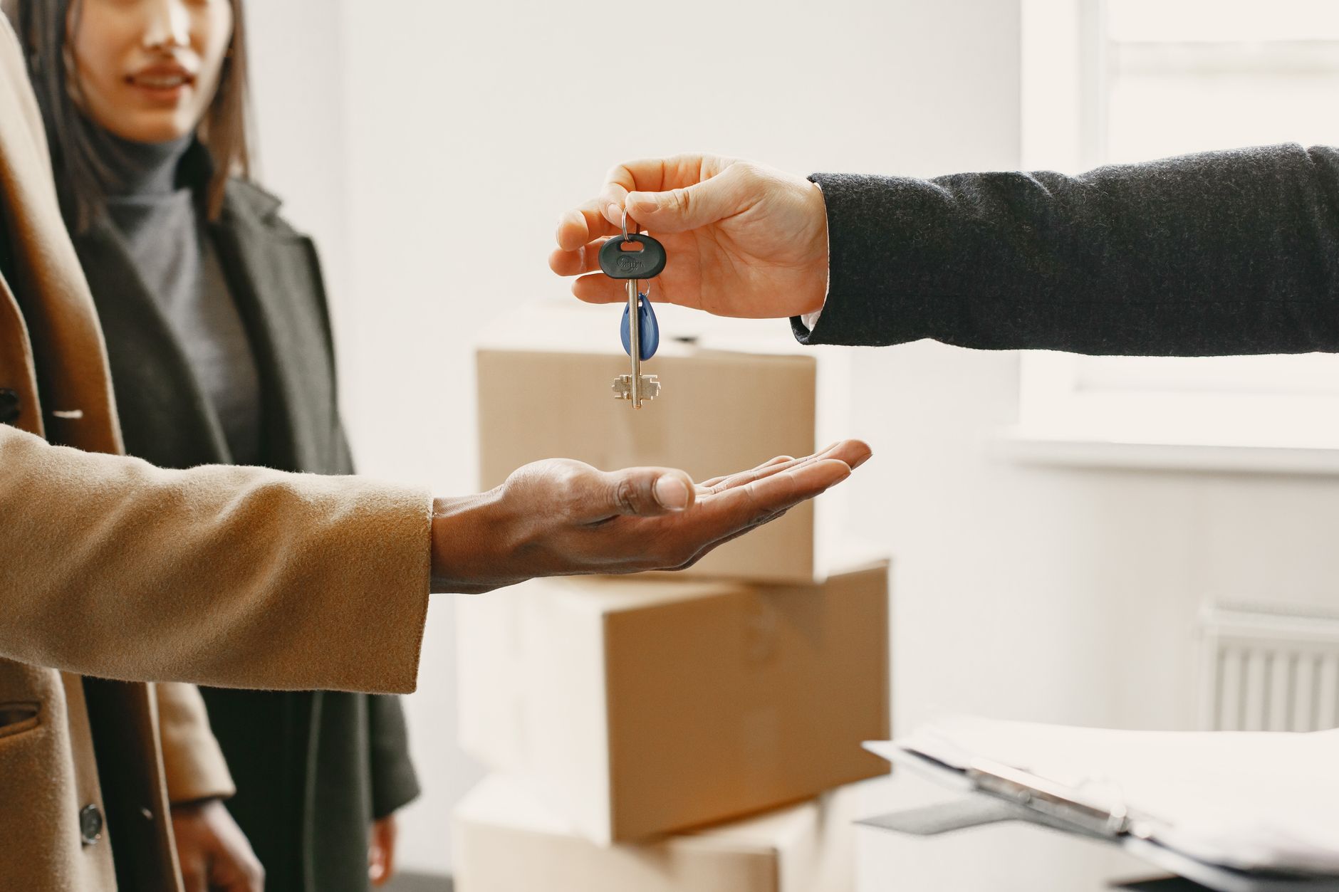 A hand passes a set of apartment keys to a new tenant standing beside moving boxes