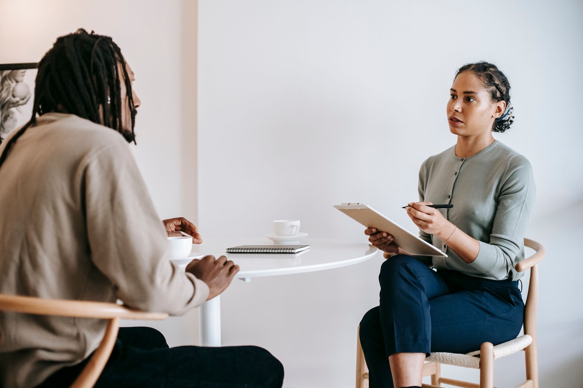 An officer with a clipboard interviews a man across a small round table in a bright office