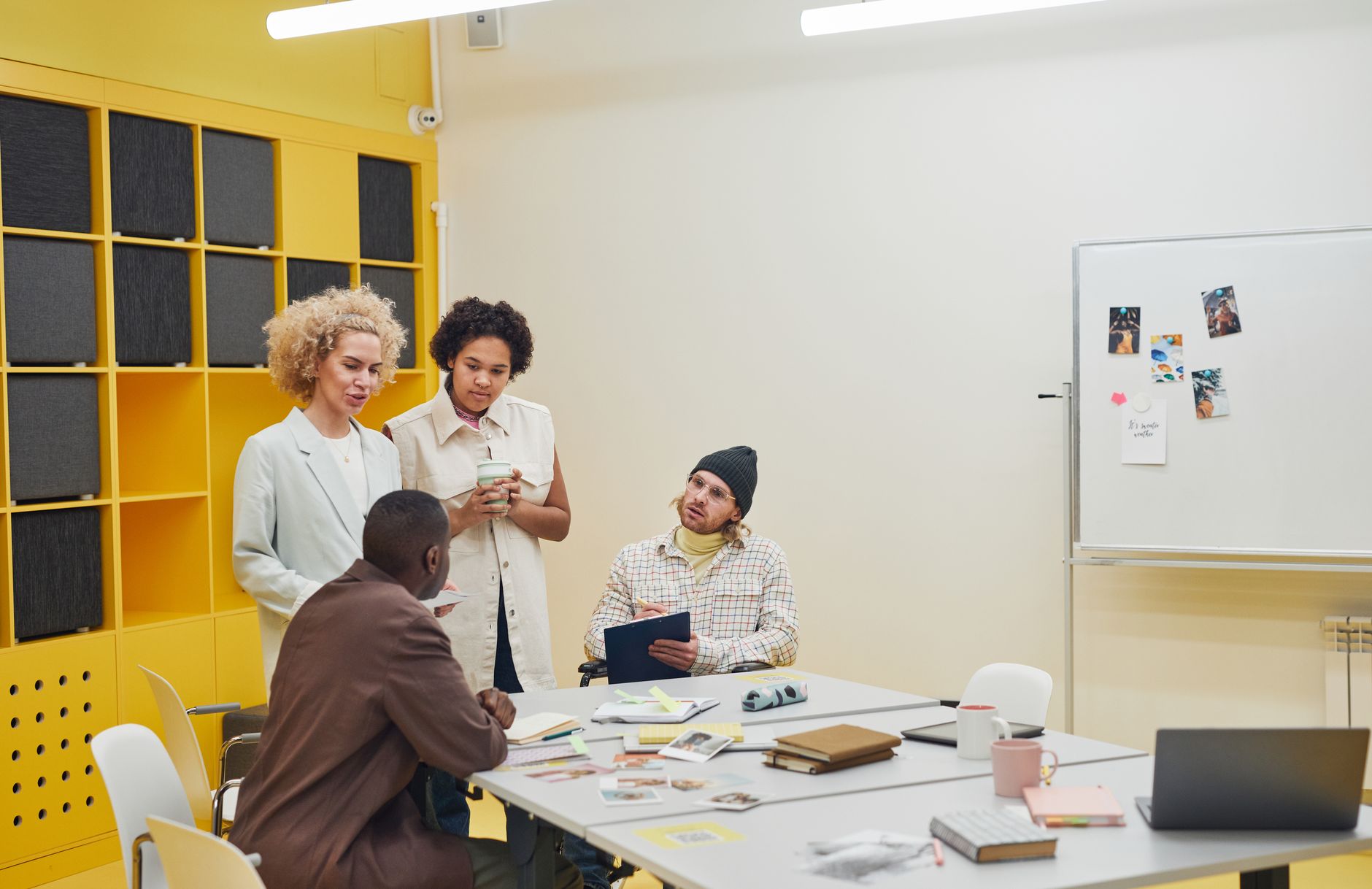 Four colleagues gather around a table with notebooks and a clipboard during a planning meeting in a bright office