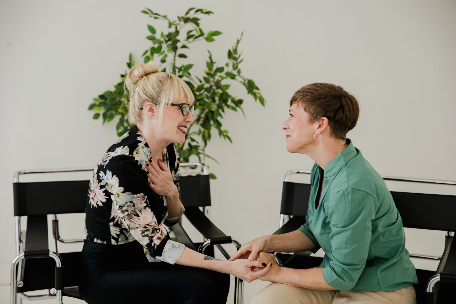 An advocate in a green shirt holds the hands of a woman in a floral jacket as they talk in two chairs