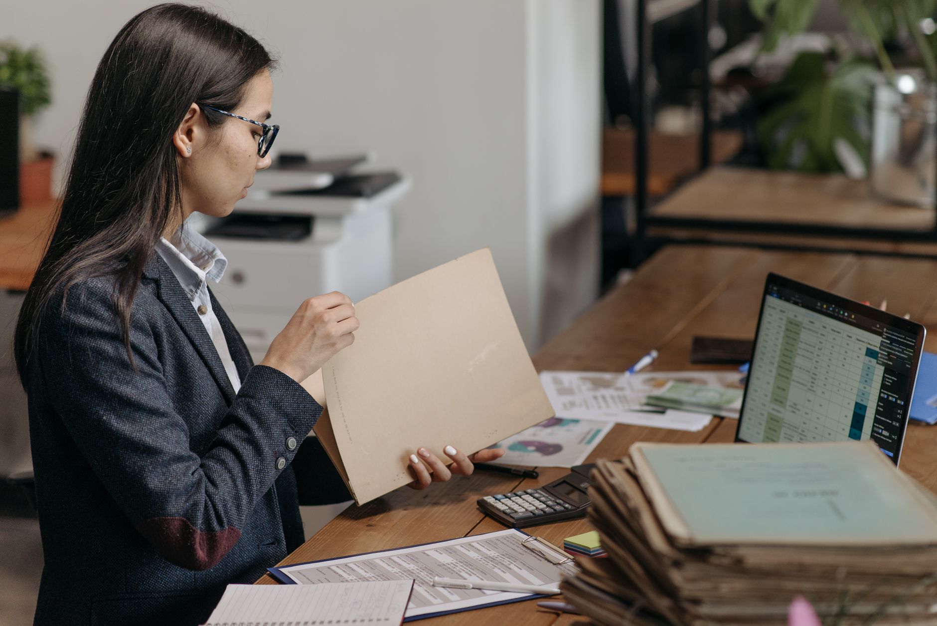 Caseworker at an office desk reading a case file beside a stack of folders and a laptop