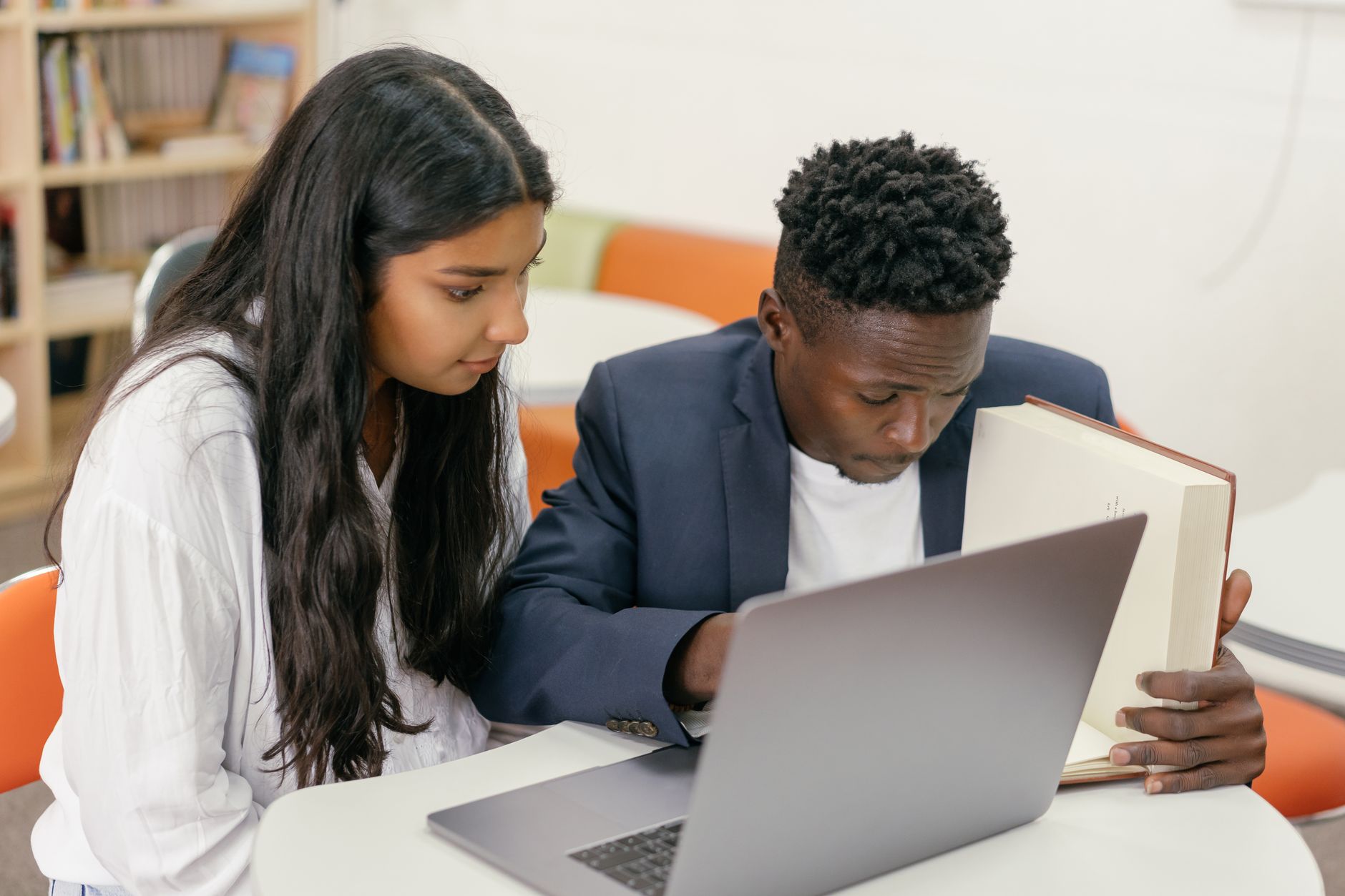 A student and an instructor review coursework together on a laptop at a table in a campus study room