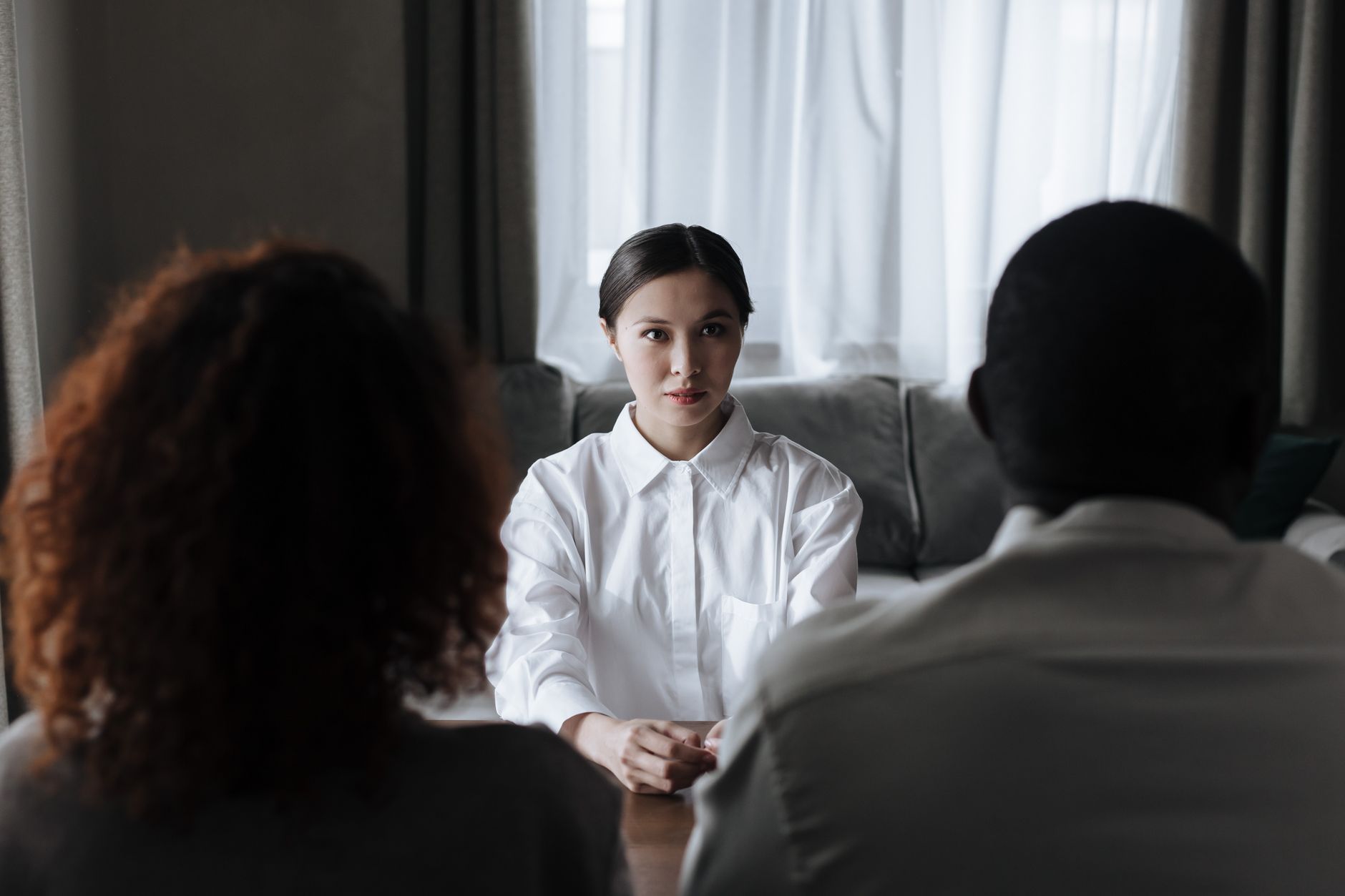 A social worker in a white shirt sits across a table from a couple during a home visit