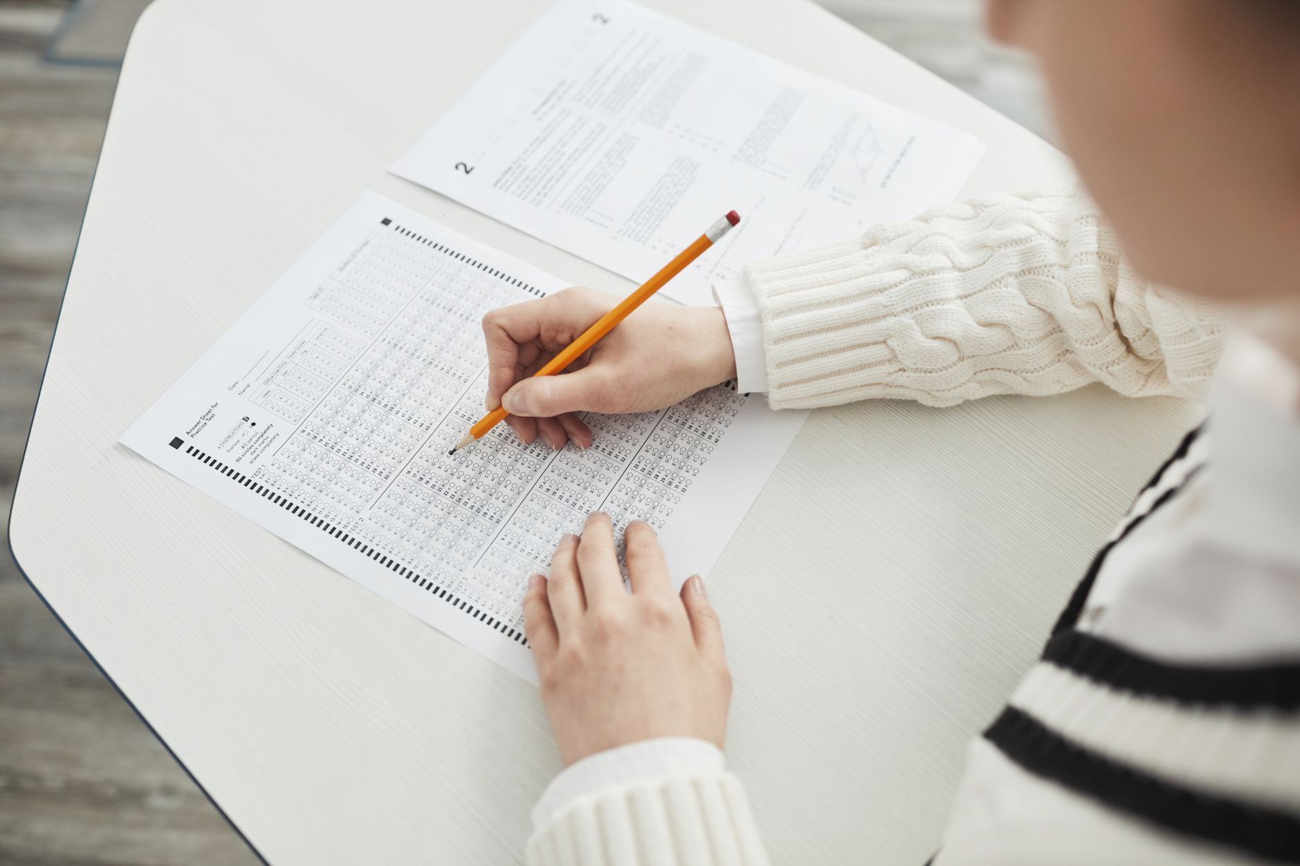A test-taker fills in a multiple-choice answer sheet with a pencil at a desk